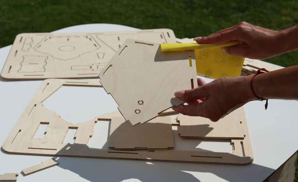 Lightly sanding a plywood bird feeder part before assembly
