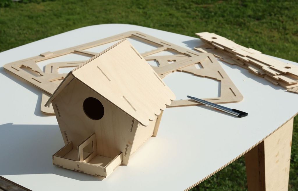 Finished plywood bird feeder beside the remaining packaging sheets and utility knife